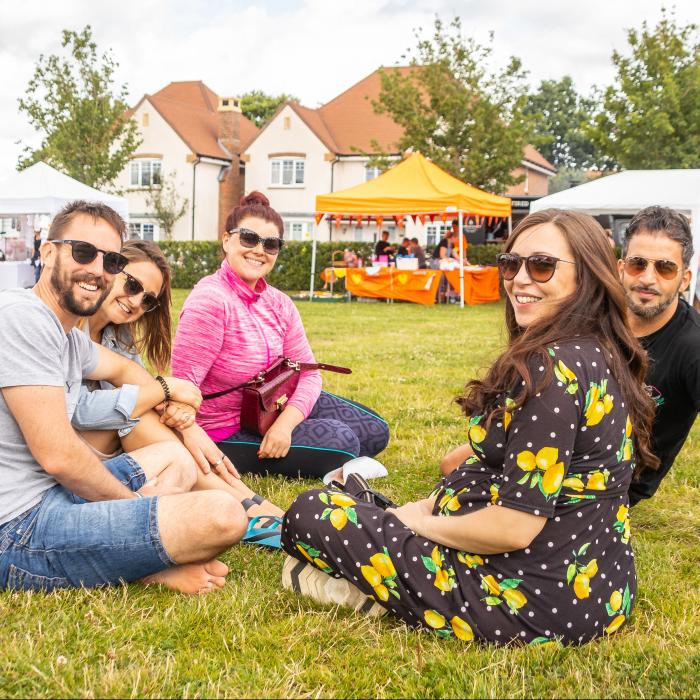 4 people at a community event sitting on the grass and smiling at the camera